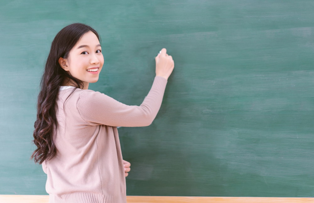 Portrait,Of,Smiling,Asian,Teacher,Woman,Writing,On,Chalkboard,,Teach