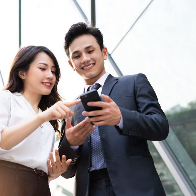 Two,Asian,Business,People,Using,Smartphone,And,Talking,Together